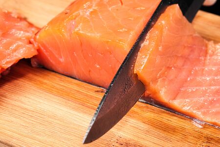 Hands cooks close-up. The chef cuts with a knife a red fish, smoked salmon on a wooden cutting...
