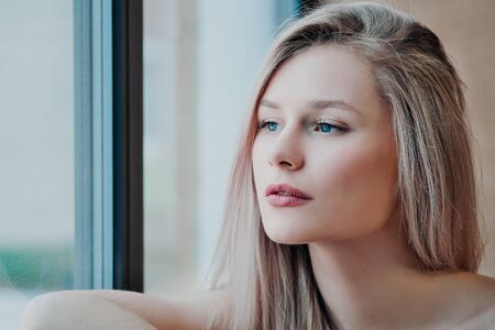Young beautiful athletic woman blonde in sportswear sitting by the window of a cafe against the background of a wooden wall. Looks out the window, smiles and stretches.の写真素材