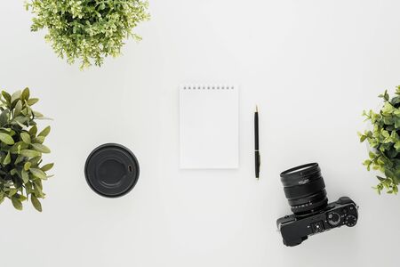 Mocap work photographer on a white table. Flat lay mirrorless camera, a few lenses and a notebook with a pen. Green pot plants. Minimalism.の写真素材