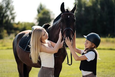 Mother and daughter riders and jockeys on a green field hug a brown horse. Mentor and student.の写真素材