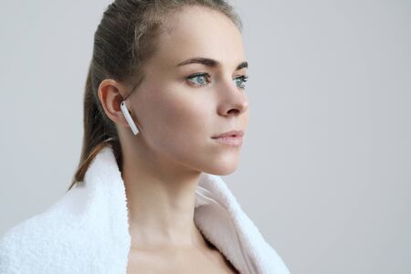 Sporty blonde girl with a white towel around her neck, in red sportswear and with white wireless...