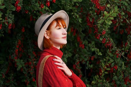 Portrait of a young attractive girl with red hair in a hat and a red sweater against the background...