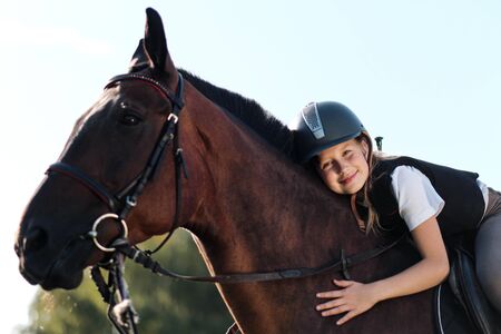 Girl teenager jockey sits on a brown horse, hugs and strokes her. Riders love of a horse.の写真素材