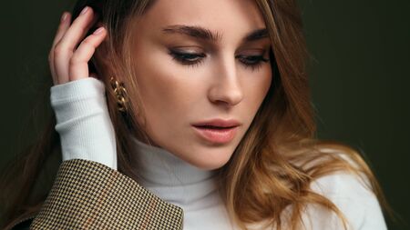 A young beautiful blonde woman in a white turtleneck and a mans jacket poses on a green olive...