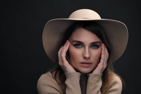 A young   woman with a beautiful face and clear natural skin poses in the studio against a black...