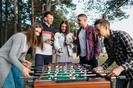 Friends play table football or kicker outdoors. A party in nature. Players and fans rejoice in the...