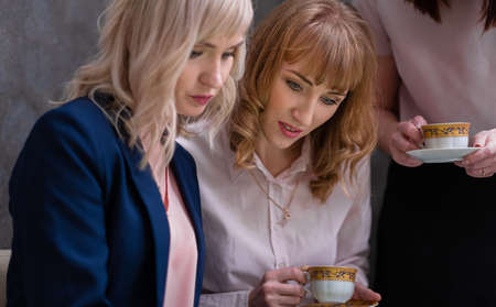 Three young women socialize and drink tea at work. Grey wall and copy space.の写真素材