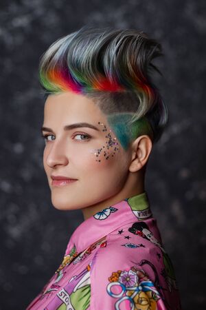 Portrait of a young beautiful girl in a pink shirt on a gray background with dyed hair. Short...