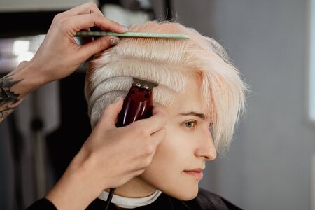 Hairdresser machine cuts woman client. A short haircut, shaved temple and a drawing on the hair....