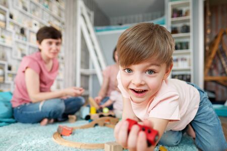 A young gay lesbian family with two children, a son and a daughter, spend time at home. They sit on the floor and play with childrens toys. The boys face is close-up.の写真素材