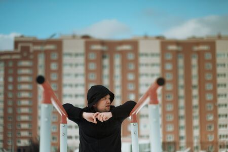 Caucasian young man is engaged in fitness and sports in winter outdoors. Street workout. The athlete trains on a street turnstile in black sportswear.の写真素材