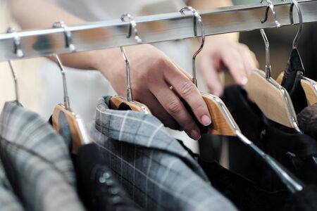Close-up of the hands of a woman choosing clothes on a hanger in a store. Female consumer buys dress...