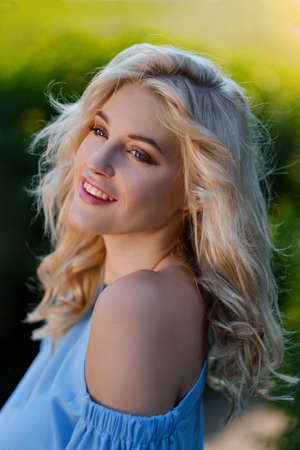 Portrait of a young beautiful girl 21 years old in a blue summer dress with a white belt bag. The woman smiles. Beautiful lips and eyes. Long loose hair, natural beauty.の写真素材