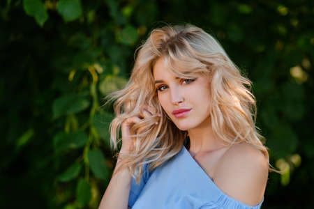 Portrait of a young beautiful girl 21 years old in a blue summer dress with a white belt bag. The woman smiles. Beautiful lips and eyes. Long loose hair, natural beauty.の写真素材