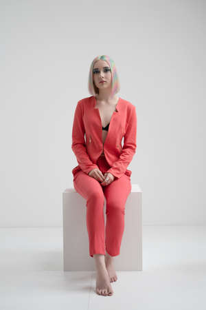 Portrait of a young beautiful informal blonde girl with dyed hair. Red jacket suit on the naked body. Studio photoshoot on a white background. Creative makeup.の写真素材