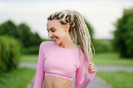 A young beautiful woman in a pink T-shirt with white dreadlocks outdoors. Girl smiles and laughs.の写真素材