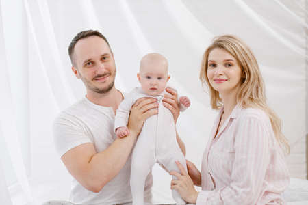 A young Caucasian family with a newborn baby daughter in the bedroom. White light home interior. They laugh and hug.の写真素材