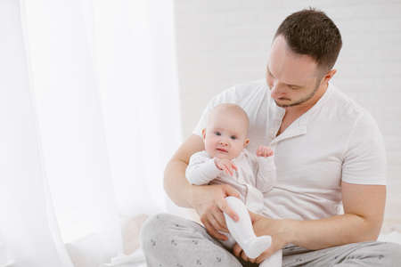 A young father holds a newborn baby daughter. White background, home interior.の写真素材