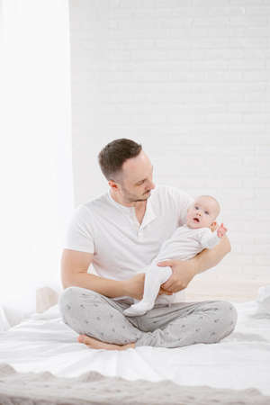 A young father holds a newborn baby daughter. White background, home interior.の写真素材