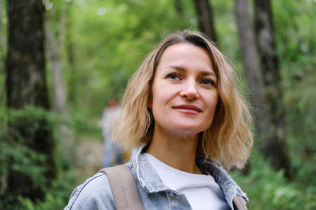 A young Caucasian woman walks along a forest mountain road. Casual blue denim clothes and backpack. Travel, healthy lifestyle and freedom.の写真素材