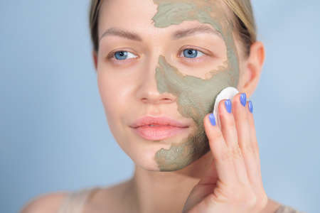 Close-up of the face of a young caucasian blonde woman. Green beauty mask made of clay on the face. Cosmetic procedure, rejuvenation and skin care.の写真素材