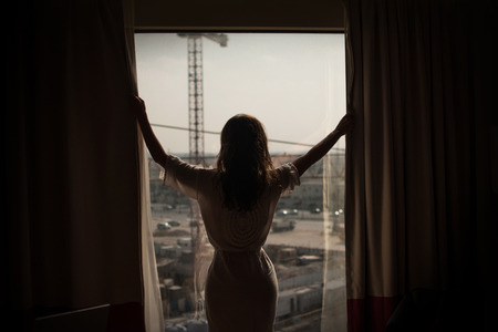 Young businesswoman opening curtain and looking on industrial in center city view.の写真素材