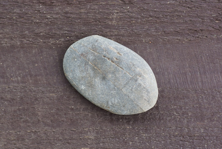 A flat stone lying on a wooden surface. Close-up.