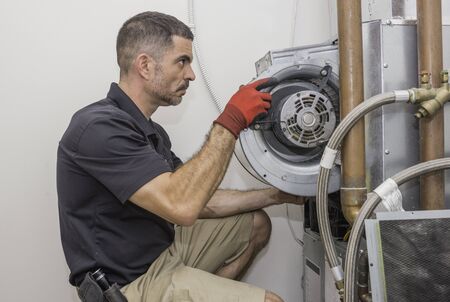 HVAC technician removing a furnace blower motor from a commercial heat pump. Repair man wearing a...