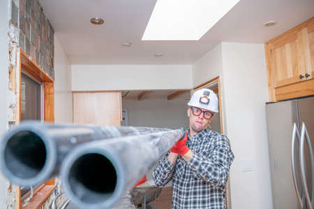 Construction worker inside unfinished home kitchen holding PVC pipe.