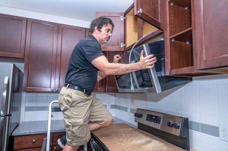 Appliance technician on a step ladder installing a over the range microwave to a cabinet
