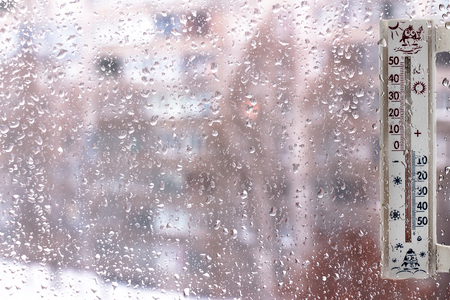A thermometer on windows covered with raindrops, as a symbol of bad weatherの写真素材