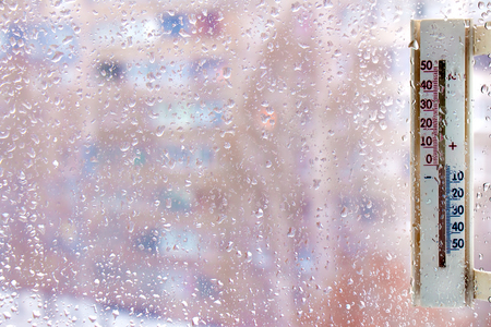 a thermometer on windows covered with raindrops, as a symbol of bad weatherの写真素材