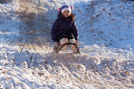 Happy and excited girl Sledding downhill on a snowy day.Cute girl laughing and showing excitement while she slides downhill while snow sledding on a winter day outdoorsの写真素材