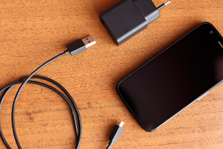 Mobile phone with connected plug of charger, smartphone charging on tableの写真素材