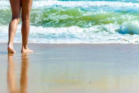 Feet girl barefoot walking by the sea. The girl touches the foot of the water.の写真素材