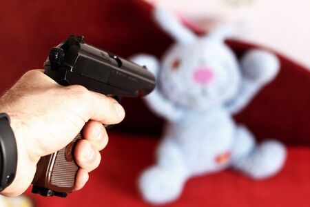 The toy rabbit is threatened with a gun. The rabbit holds his hands up.の写真素材