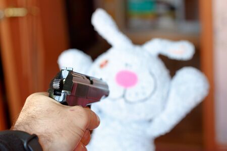 The toy rabbit is threatened with a gun. The rabbit holds his hands up.の写真素材