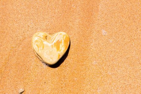A heart-shaped stone lies on the sand as a symbol of love.の写真素材