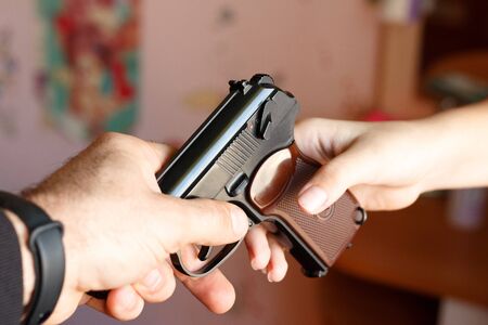 Adult man hands a gun to a childの写真素材