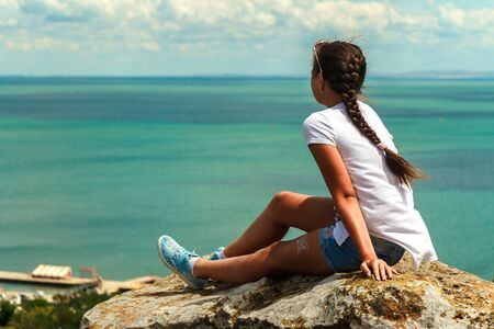 Beautiful young girl sits enjoying the sea view.の写真素材