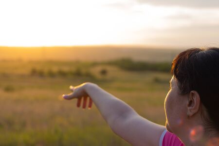 The girl shows the beautiful nature and sunny sunset.の写真素材