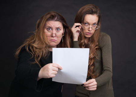 two shocked women with paper sheet over black backgroundの写真素材