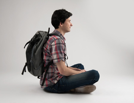 man with backpack sitting isolated over gray backgroundの写真素材