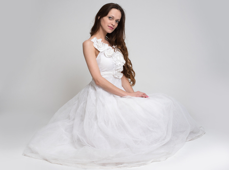 beautiful brunette woman in white dress on gray backgroundの写真素材