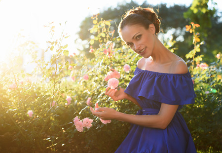 Beautiful girl in blue dress relaxing in a rose gardenの写真素材