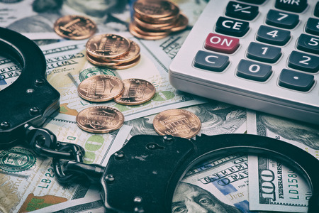 tax offense concept. Us dollars and handcuffs on table. Money, coins and calculatorの写真素材