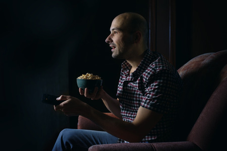 guy watching TV with remote control at home at nightの写真素材