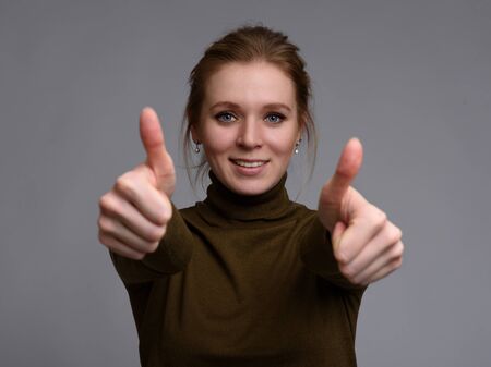 Happy young woman giving thumbs up on grey backgroundの写真素材