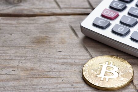 bitcoin coin and calculator on an old wooden deskの写真素材