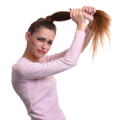 Sad girl holds her damaged hair. Isolated on whiteの写真素材